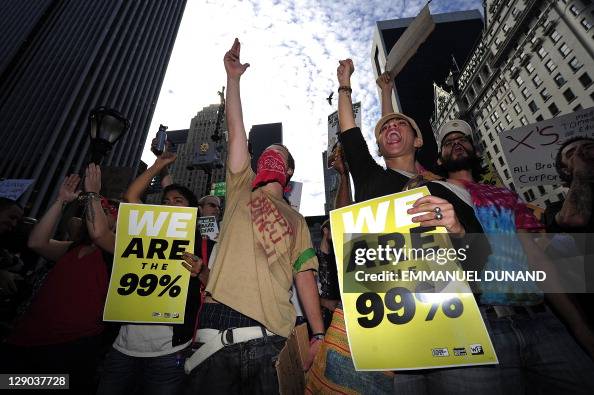 Getty images photo of a group of protestors with a young man in the center wearing a red bandana. Two protestors to each of his sides hold placards reading WE ARE THE 99%