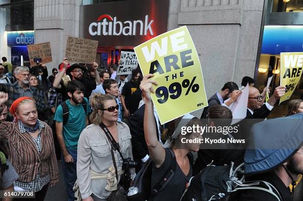 Getty images photo of a group of protestors with a young woman in the center holding up a placard reading WE ARE THE 99%