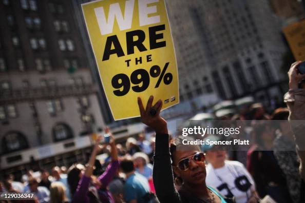 Getty images photo of a crowd of protestors with a woman in the center foreground holding a placard reading WE ARE THE 99%