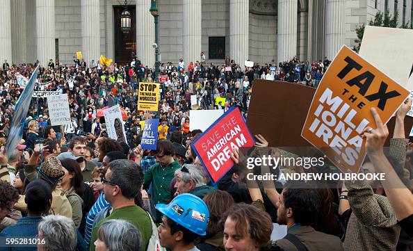 Getty images photo of a crowd of protestors. One protestor in the right foreground holds a placard reading TAX THE MILLIONAIRES