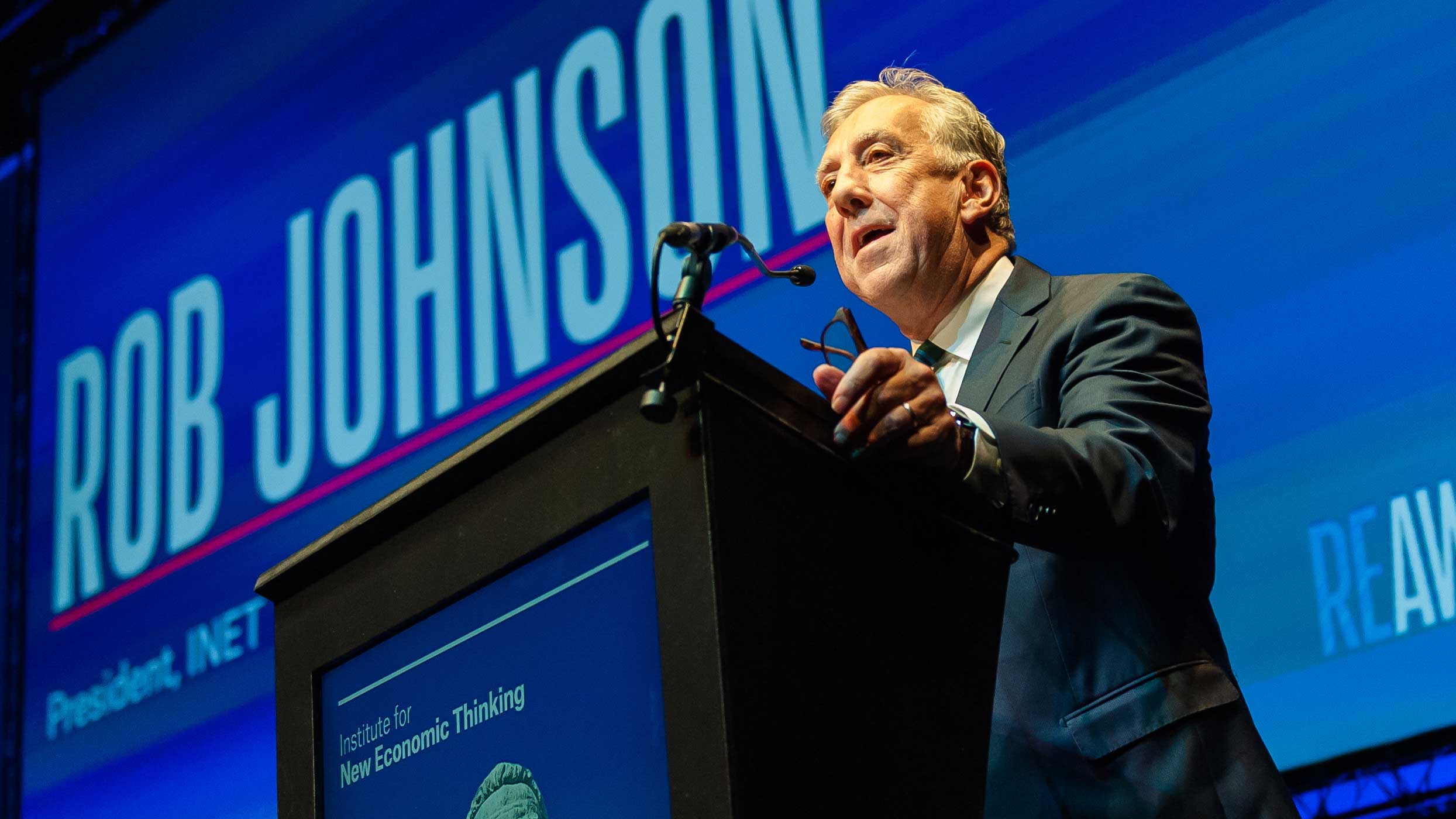 Rob Johnson speaking at the Reawakening conference with branded projected backdrop and lectern screen