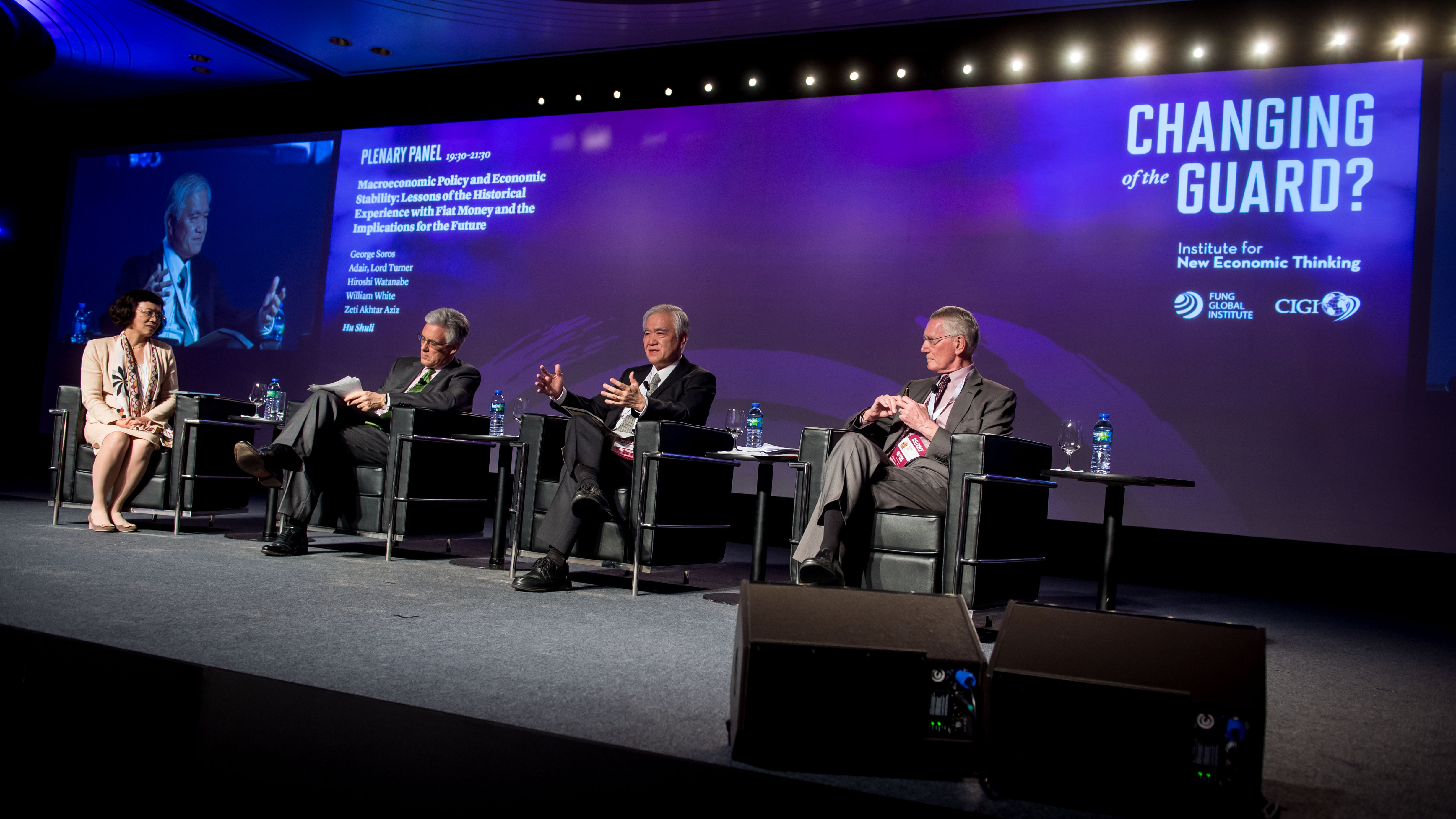 A panel discussion at the Changing of the Guard conference, including a view of the branded digital screen in background with panel and conference information