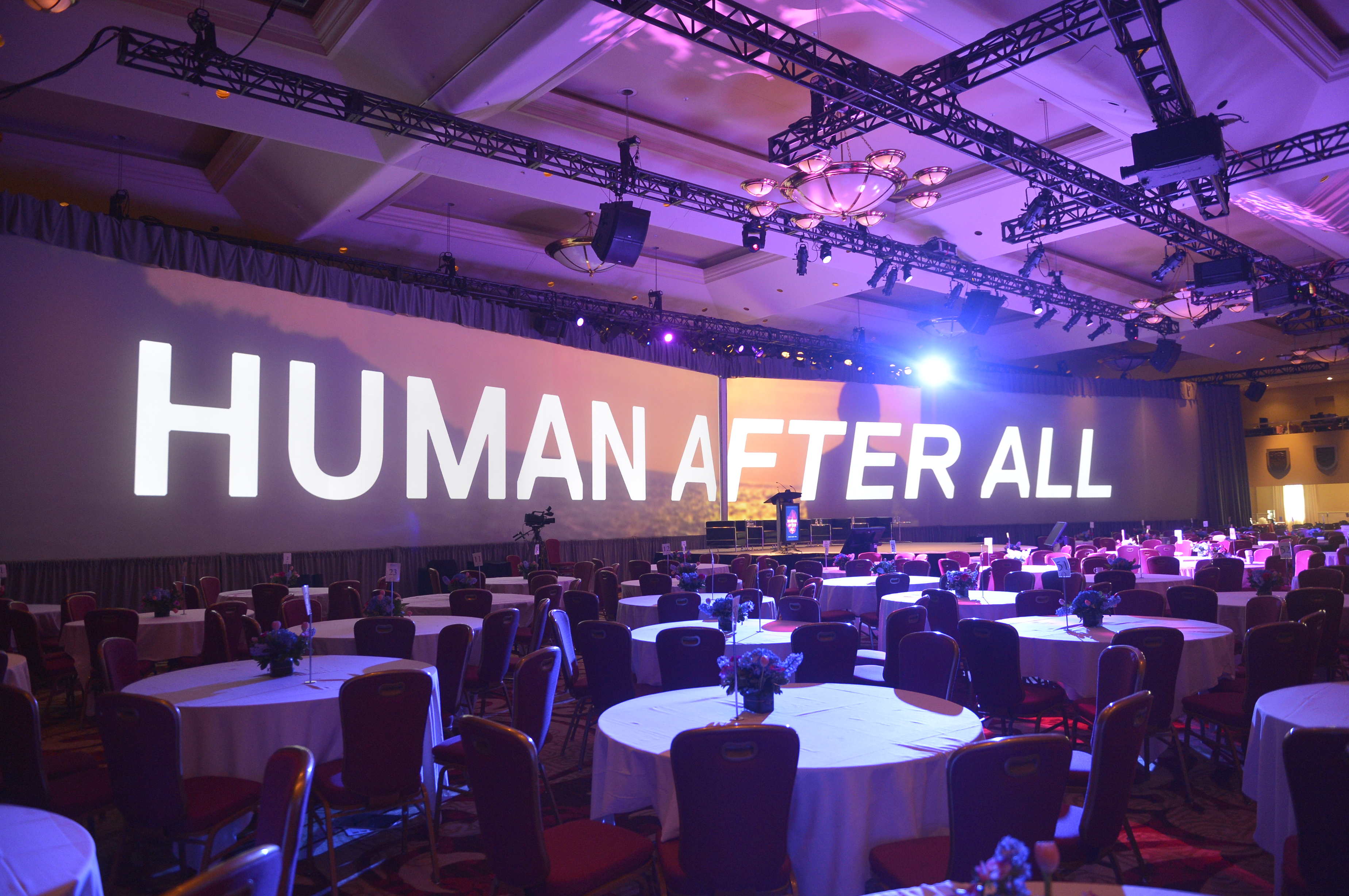 Conference dining hall with Human After All branding projected across wide screens in background