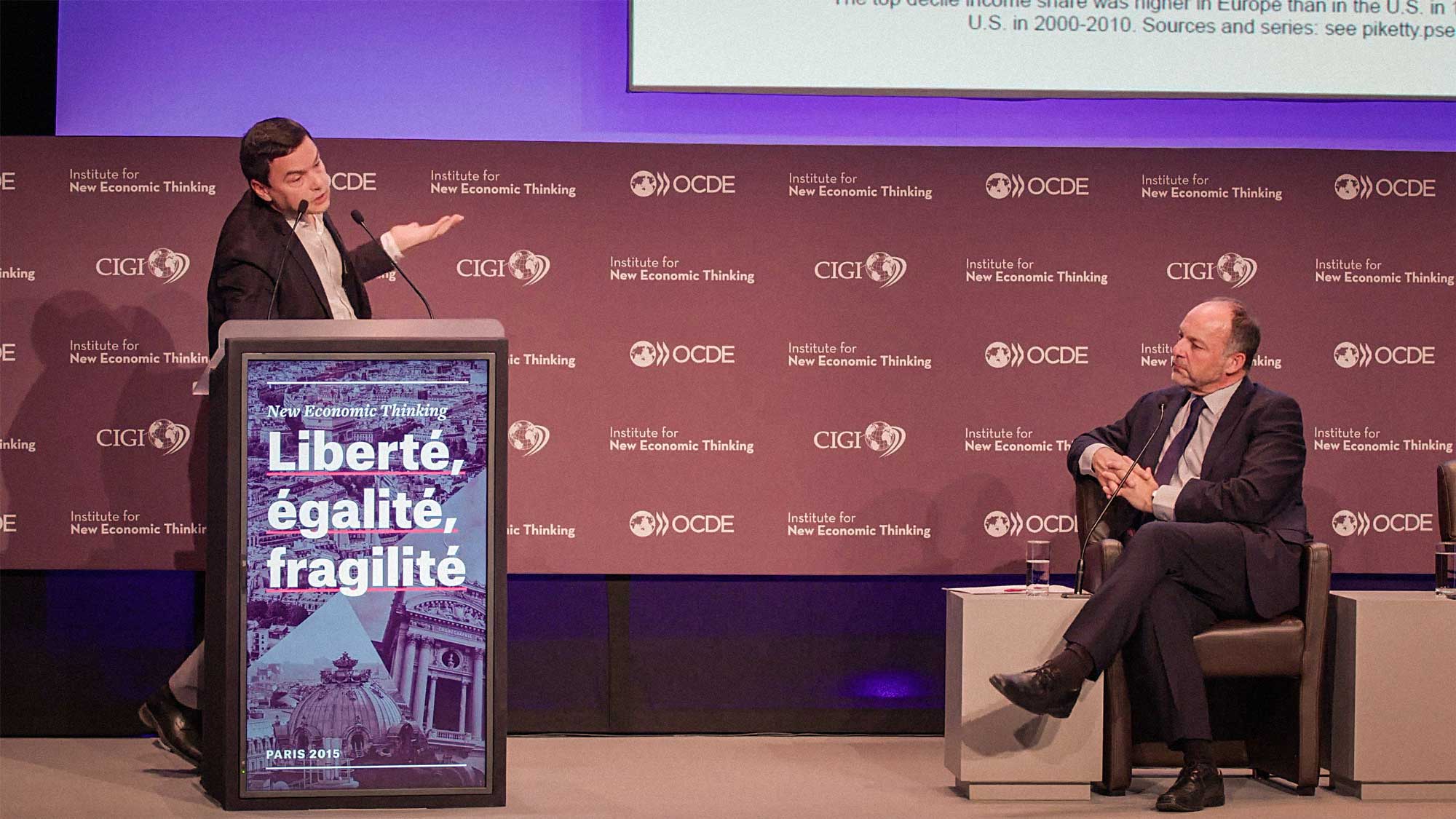 Thomas Piketty speaking at the Liberté, egalité, fragilité conference with branded lectern in foreground and branded step and repeat in background