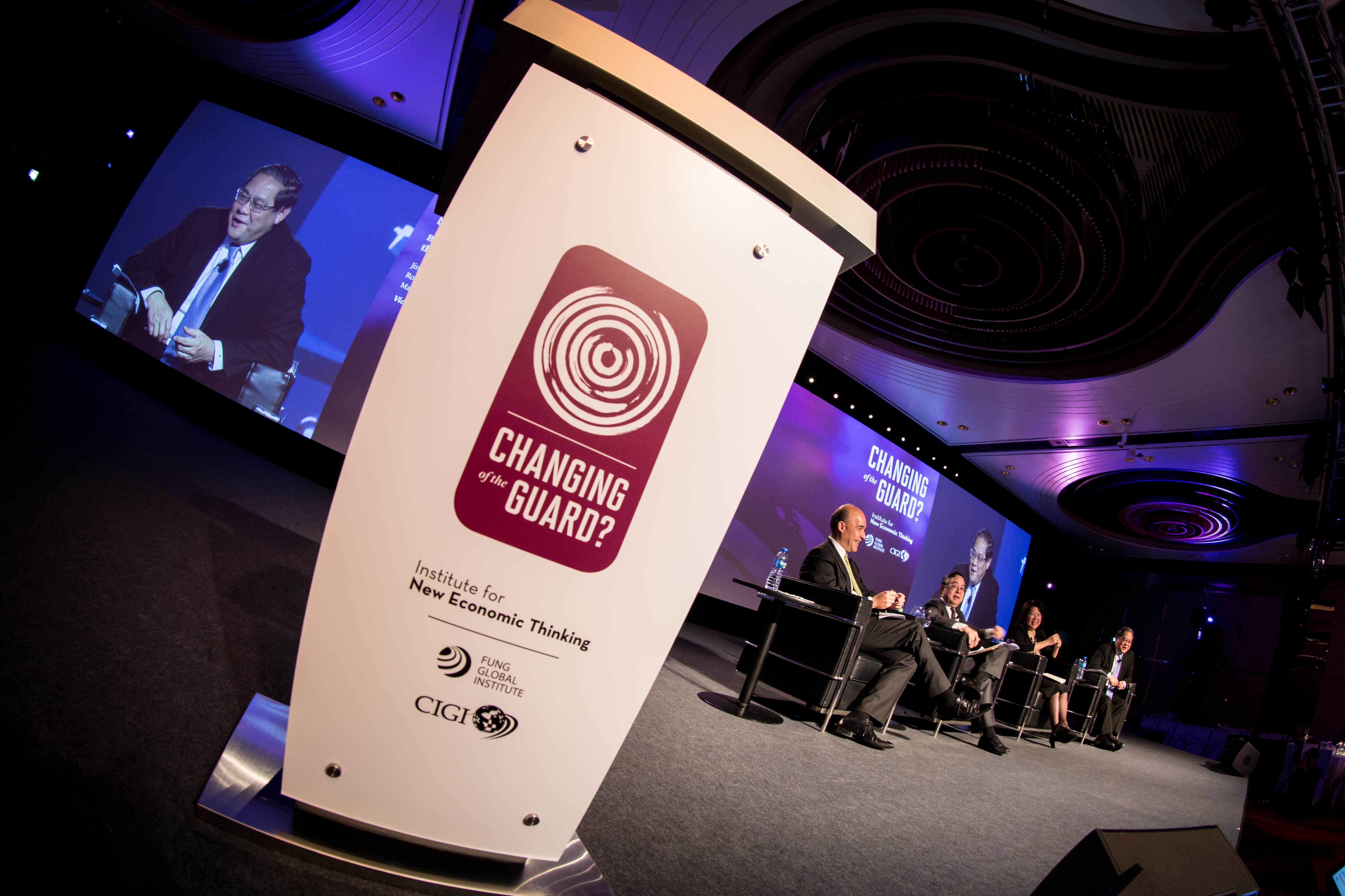 Closeup of the branded lectern at the Changing of the Guard conference with a panel discussion and branded digital conference screen in the background